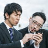 渋い顔でスマホを覗き込む会社員の写真